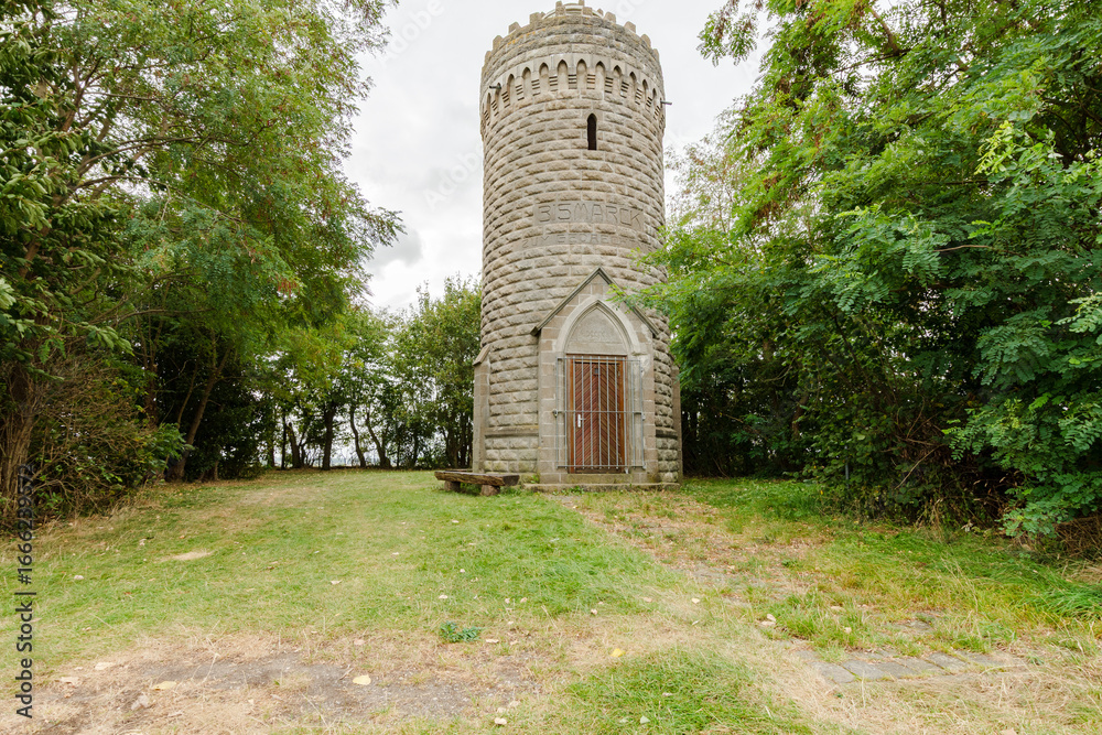Naklejka premium Der historische Bismarckturm steht inmitten von Bäumen und Grünflächen. Seine markante Steinarchitektur mit Tor und Zinnen hebt sich klar vom umgebenden Naturraum ab.