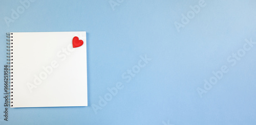 Spring-loaded notebook with square white sheets and a red heart on a blue background. Notebook Blank for Notes, Space for Copy, Text and Advertising, Banner, School Notebook, Business, Blank Sheet