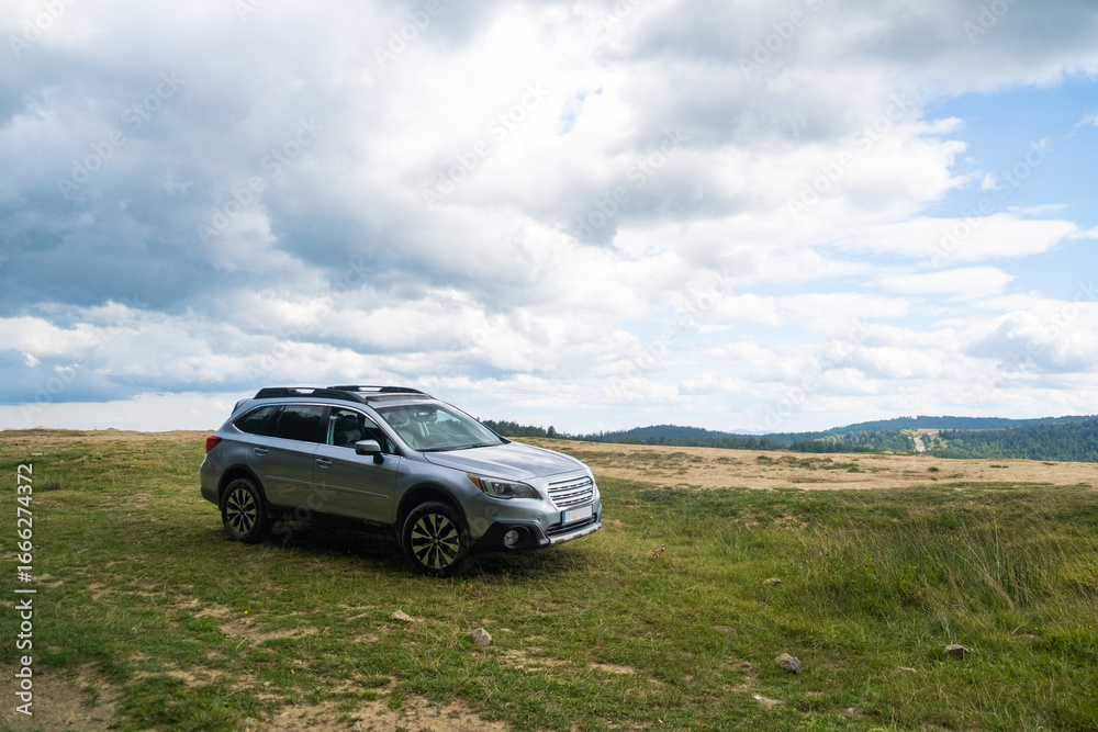 Fototapeta premium Silver SUV on Grassy Hill with Cloudy Sky