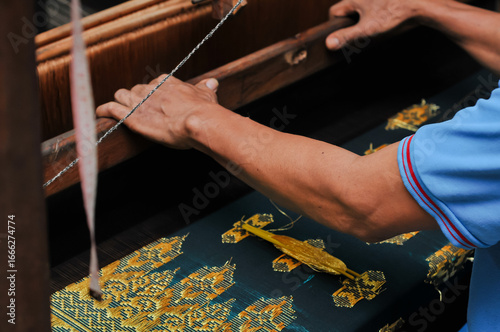 Tableau sur toile Close up of artisan hands weaving traditional fabric on a wooden loom with golden thread