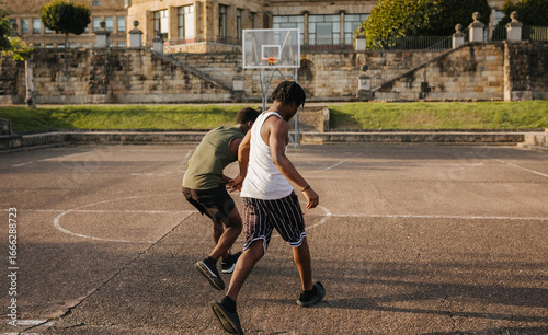 Two teen guys playing street basketball on old urban court at sunset