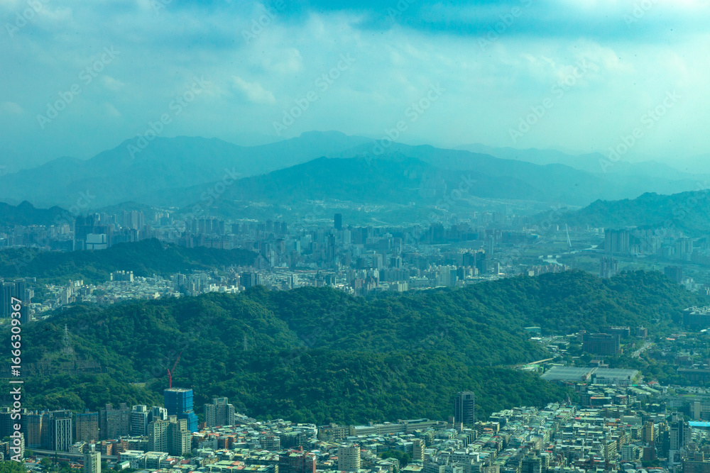 Obraz premium Panoramic view of Taipei City with distant mountains, showing a blend of dense urban structures and lush green hills under hazy blue skies