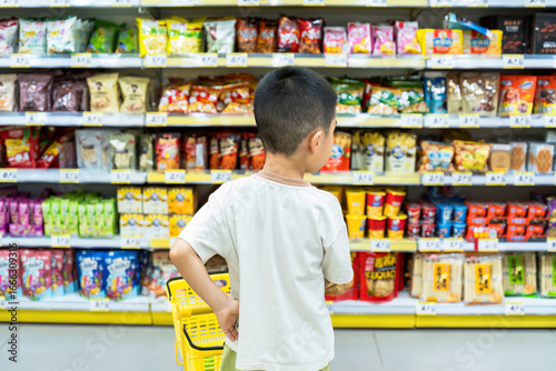 Fotografía A young boy is seen from behind standing in a supermarket aisle surrounded by various snack products on the shelves