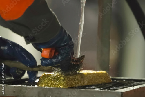 Washing and cleaning with metal brush of a gold bar after smelting.