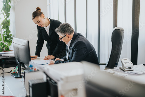 Fototapete Two business people are working together in a modern office environment, discussing documents
