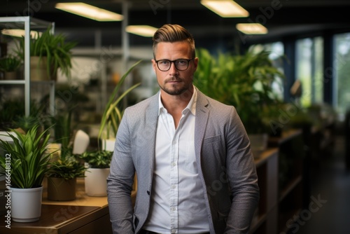 Wallpaper Mural A man with glasses and styled hair poses in a contemporary office environment filled with greenery. The warm ambiance reflects a productive work atmosphere Torontodigital.ca
