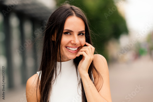 Elegant young woman with a charming smile outdoors in a city, showcasing a stylish and confident lifestyle on a sunny day