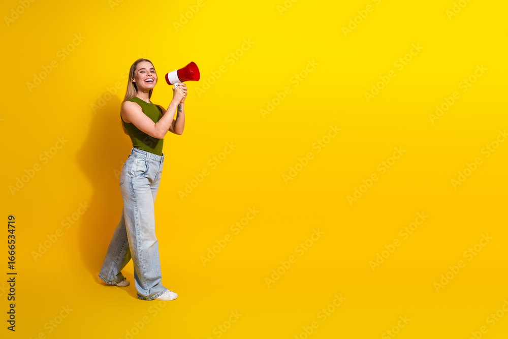 Fototapeta premium Excited young woman with megaphone in casual outfit posing against vivid yellow background, radiating joyful energy