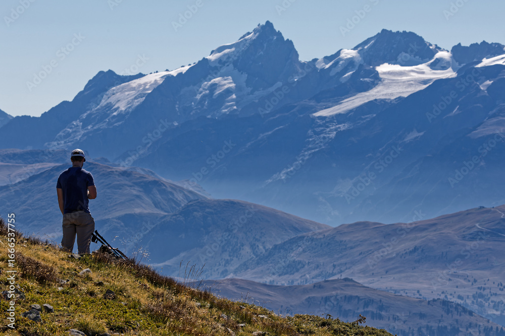 Fototapeta premium CHAMROUSSE, FRANCE, August 24, 2025 : Mountaineer at the Col des Vans summit point of view admire the view on Oisans massif and La Meije summit