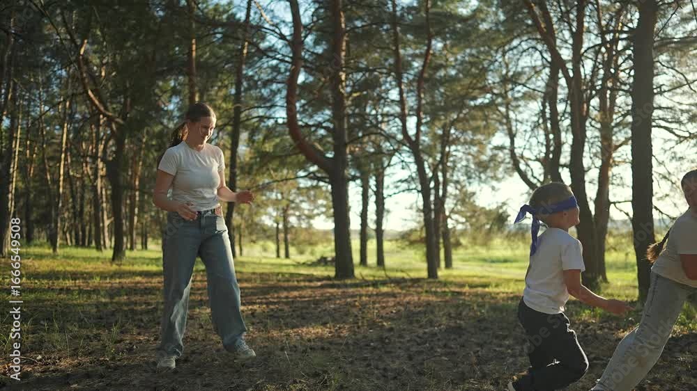 Family plays blindfold game forest clearing. Boy moves hands searching near laughing girl. Woman joins outdoors summer fun. Child explores woods wearing blindfold, family enjoys nature game. Family plays blindfold game forest clearing. Boy moves hands searching near laughing girl. Woman joins outdoors summer fun. Child explores woods wearing blindfold, family enjoys nature game.