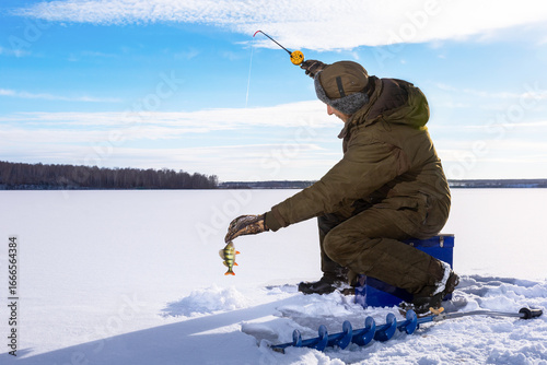 Fishman ice fishing on frozen lake at sunny winter day.