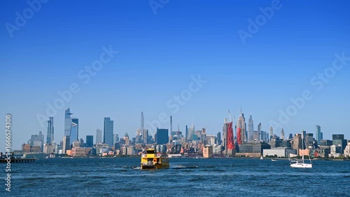 Large yellow riverboat approaches by the waterscape. Varied skyline of Manhattan on the other bank of the Hudson River. Perspective from Jersey.