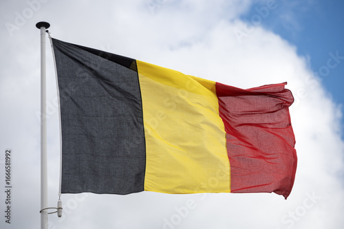 Belgium flag fluttering in the wind with a blue sky and cloud background. 
