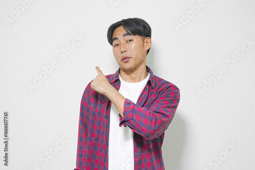 Asian man in a checkered shirt points to the upper left corner against a white background.
