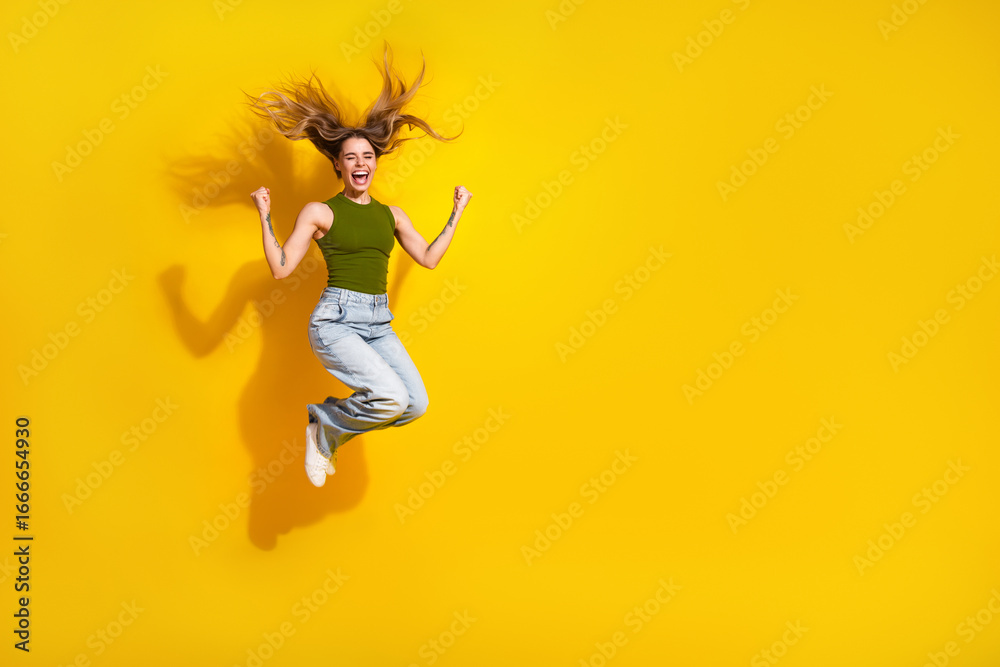 Obraz premium Cheerful young woman jumping high on a vibrant yellow background showing excitement and happiness in casual khaki attire