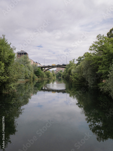 Garca Ojeda Bridge, which provides access to the Templar Castle of Ponferrada, located over the river Sil and reflected in it with many trees and vegetation on both banks of the river