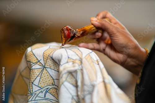Close-up of an artisan applying hot wax with a canting on patterned fabric—traditional batik making for textile design, craft tutorials, heritage and culture visuals.