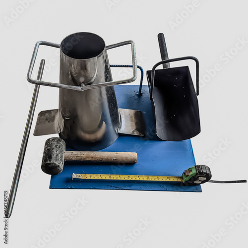 Obraz na płótnie Concrete slump test set including cone mold, tamping rod, hammer, trowel, and measuring tape on blue base, isolated on white background