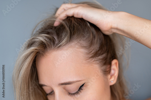 Close-up of young woman lifting her hair to reveal hairline and scalp. Concept of hair loss, alopecia, thinning hair, hair care and healthy scalp on neutral background