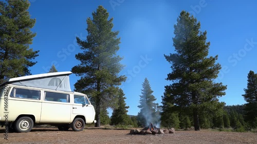 Vintage Camper Van Parked Near Campfire in Forest Under Clear Blue Sky