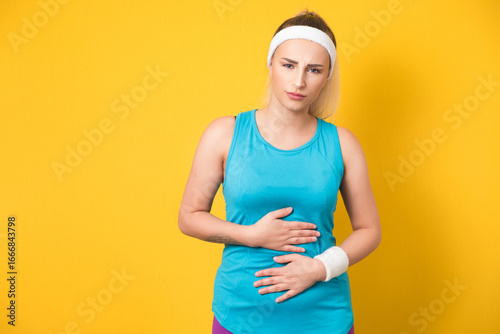 Stomach ache, fitness woman suffering from stomachache, isolated on yellow background. Ill vitality girl with chronic gastritis. Abdomen bloating concept. 80s styling