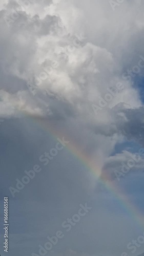 Beautiful rainbow shining through gentle rain with soft, fluffy clouds in the sky.