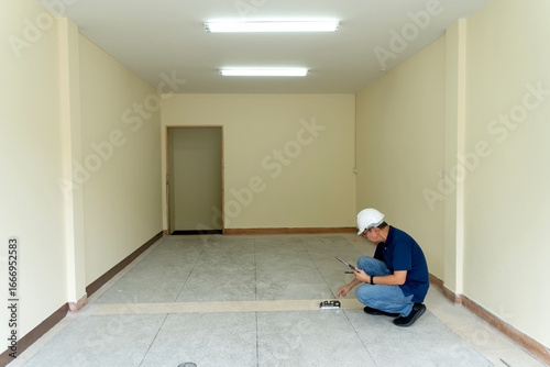 Professional Asian male adult engineer examining floor level empty room wearing hard hat checking construction site quality inspection
