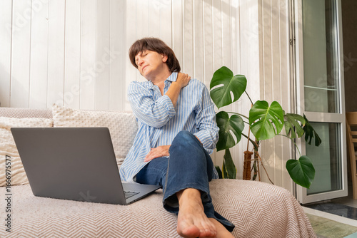 Slika na platnu Adult European woman experiencing shoulder and neck pain after working on laptop in brightly lit room