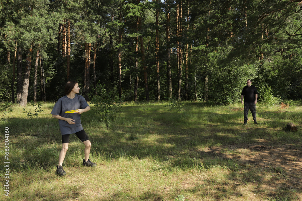 Fototapeta premium Family spending quality time together playing frisbee in open field with scenic forest view, concept of nature activities, exercise, and emotional connection between generations.