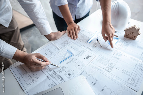 Team of architects or engineering consulting and analyzing working on objects tools and construction drawings inspection, discussing planning new architectural project on blueprint and model house