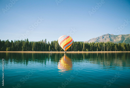 Vibrant hot air balloon over serene lake reflecting in the clear water on a sunny day
