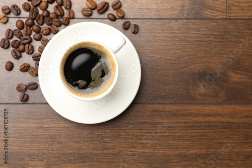 Aromatic coffee in cup and beans on wooden table, flat lay. Space for text