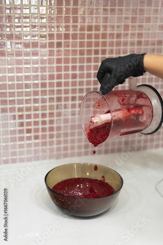 Close-up of a woman's gloved hands cooking berry jam made from fresh raspberries in the kitchen