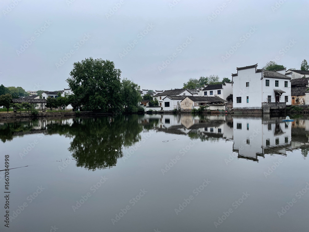 Fototapeta premium Tranquil scene of a Chinese village with traditional architecture reflecting in calm water.