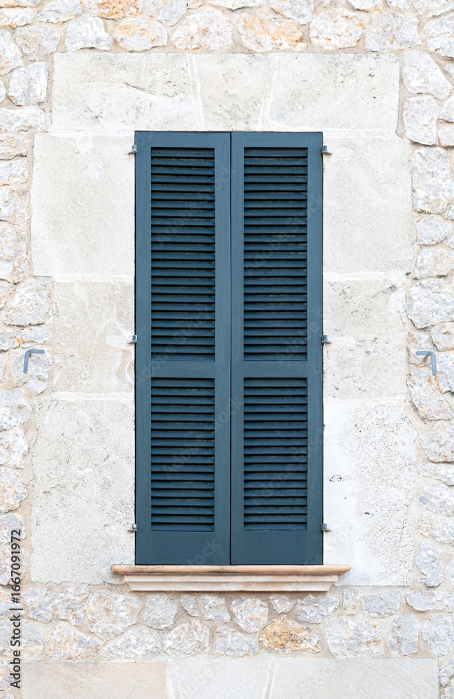 Fototapeta premium Closed blue wooden shutters on a traditional stone wall facade