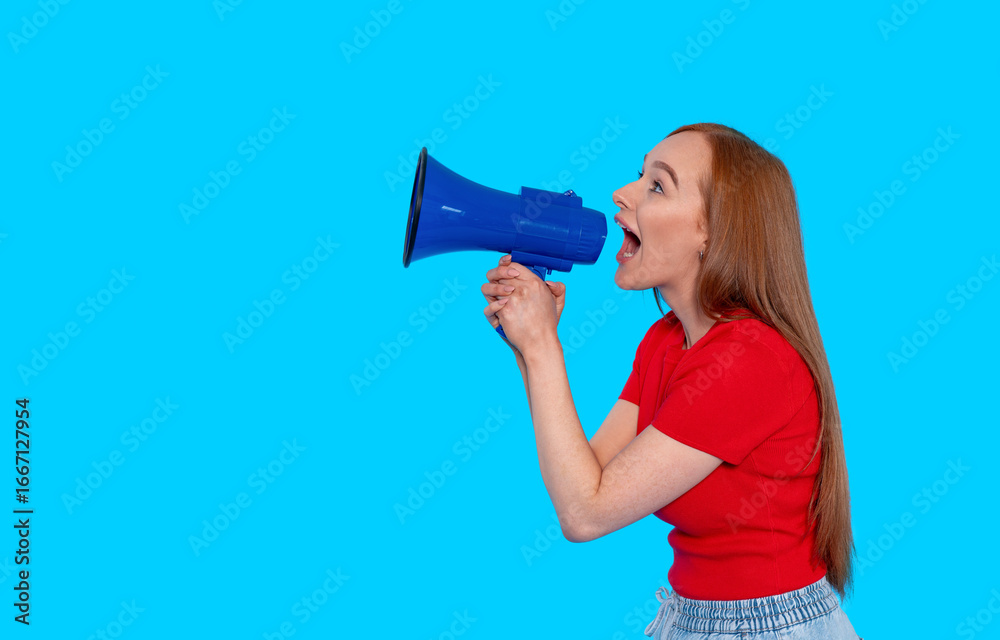 Naklejka premium Young woman enthusiastically uses blue megaphone against a bright blue background in a playful moment of expression and communication
