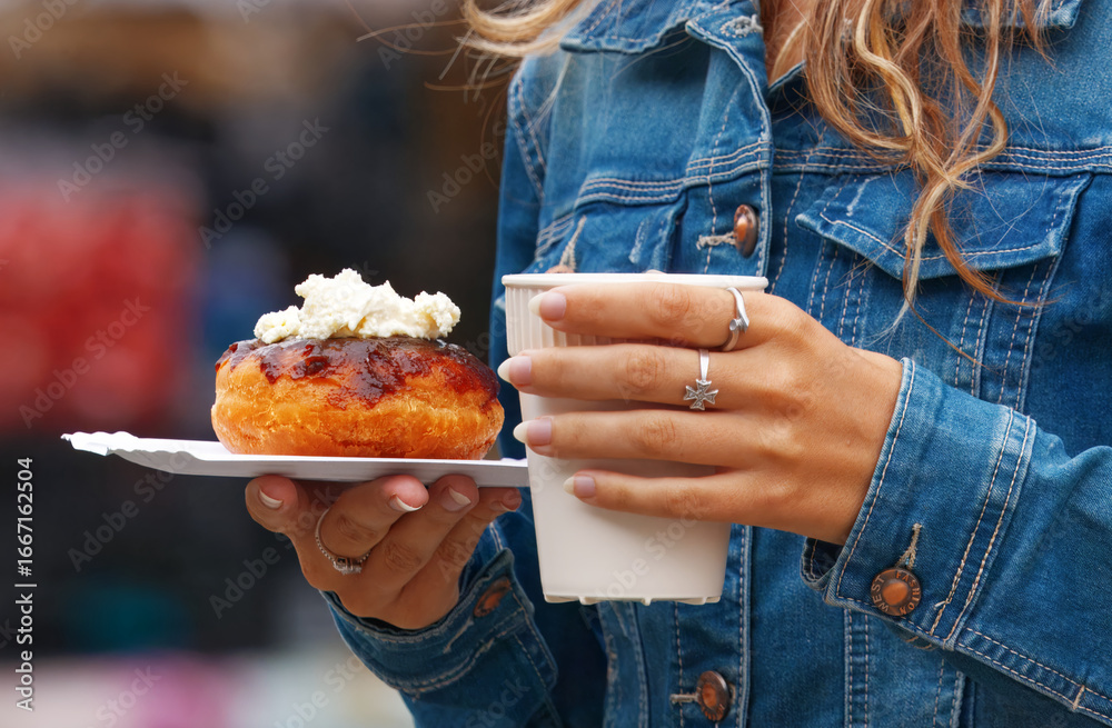 Φωτογραφία Close-up of coffee cup and sweet donut in hands of woman in blue denim jacket st