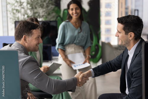 Billede på lærred Two multiethnic, young and mature male professionals shaking hands, closing commercial, profitable deal, finalize successful negotiation, or start new partnership