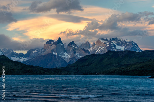 Golden hour light illuminates the iconic Cuernos del Paine peaks under a dramatic, fiery sky with lenticular clouds in Torres del Paine National Park, Patagonia.