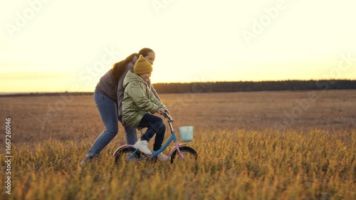 Wallpaper Mural childhood dream. woman mother teaches child to ride bike in the park. Driving lesson for kid from mom at sunset. parent helps child to keep balance and pedal. Kid learns steer bike sun. happy family. Torontodigital.ca