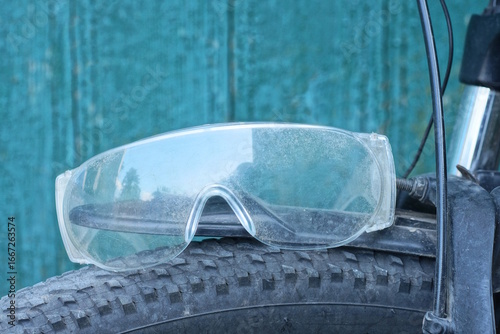 one old gray safety glasses lies on a black bicycle tire against a green wall on a summer street