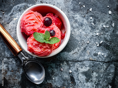 strawberry ice cream with red berries and mint in a white jar seen from above and dark background