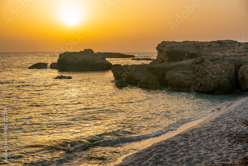 Golden sunset illuminating Punta Su Bardoni cliffs and the turquoise water of Arutas beach in Sardinia, Italy