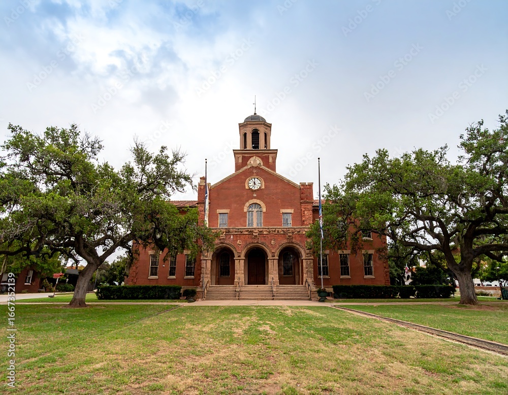 Fototapeta premium Historical Red Brick Building with Clock Tower Framed by Mature Oak Trees