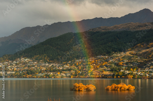 Rainbow over Queenstown lake with many houses and mountains during the autumn time