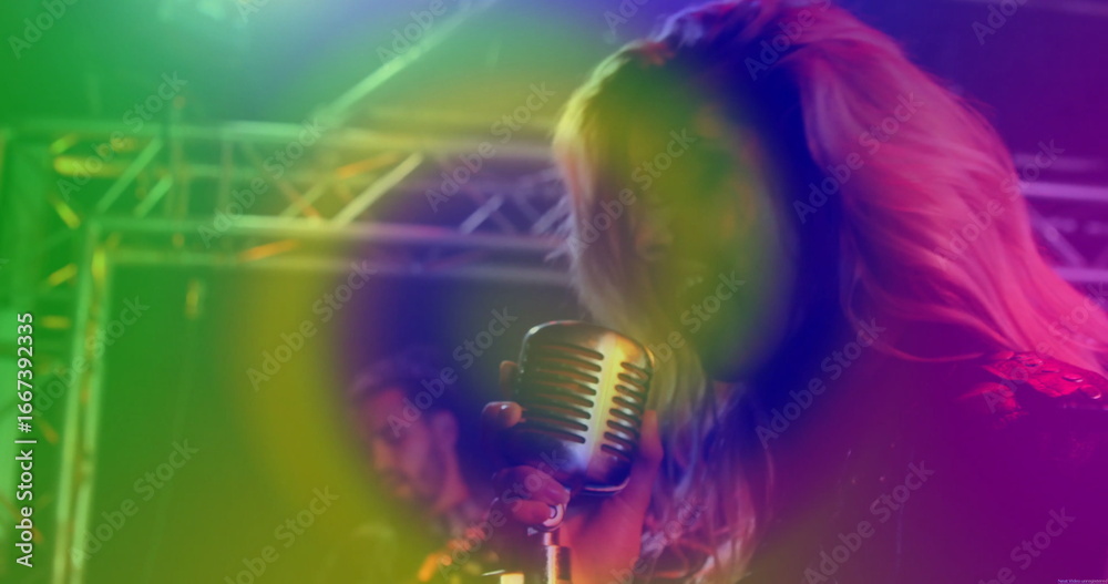 Naklejka premium Performing singer wearing leather jacket gripping microphone on stage with guitar, lights and haze