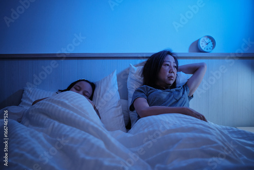 Asian single mum is sleepless, stressed, and worried awake at night after divorce near her daughter, insomnia illness in bedroom, mature and menopausal woman, family healthcare problem, lifestyle.