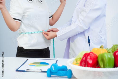 A middle-aged Asian female dietitian conducts a health consultation with a middle-aged Asian female patient at a table, focusing on weight loss, waist measurement, BMI, diet control,overall wellness