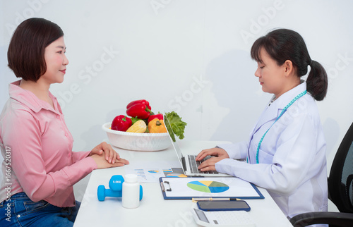 A middle aged Asian female nutritionist consults with a middle aged Asian female patient at a table, discussing nutrition, healthy eating, exercise, and lifestyle changes for weight loss and health