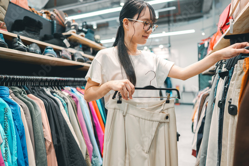 Quadro su tela Young adult woman choosing used clothing at second hand clothes shop